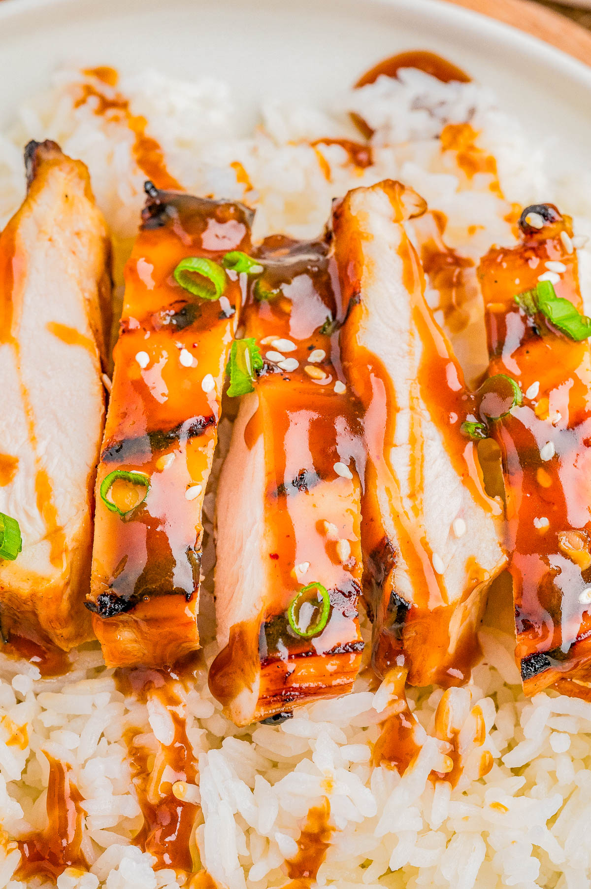 Sliced grilled chicken with teriyaki sauce and green onions served over white rice on a white plate.