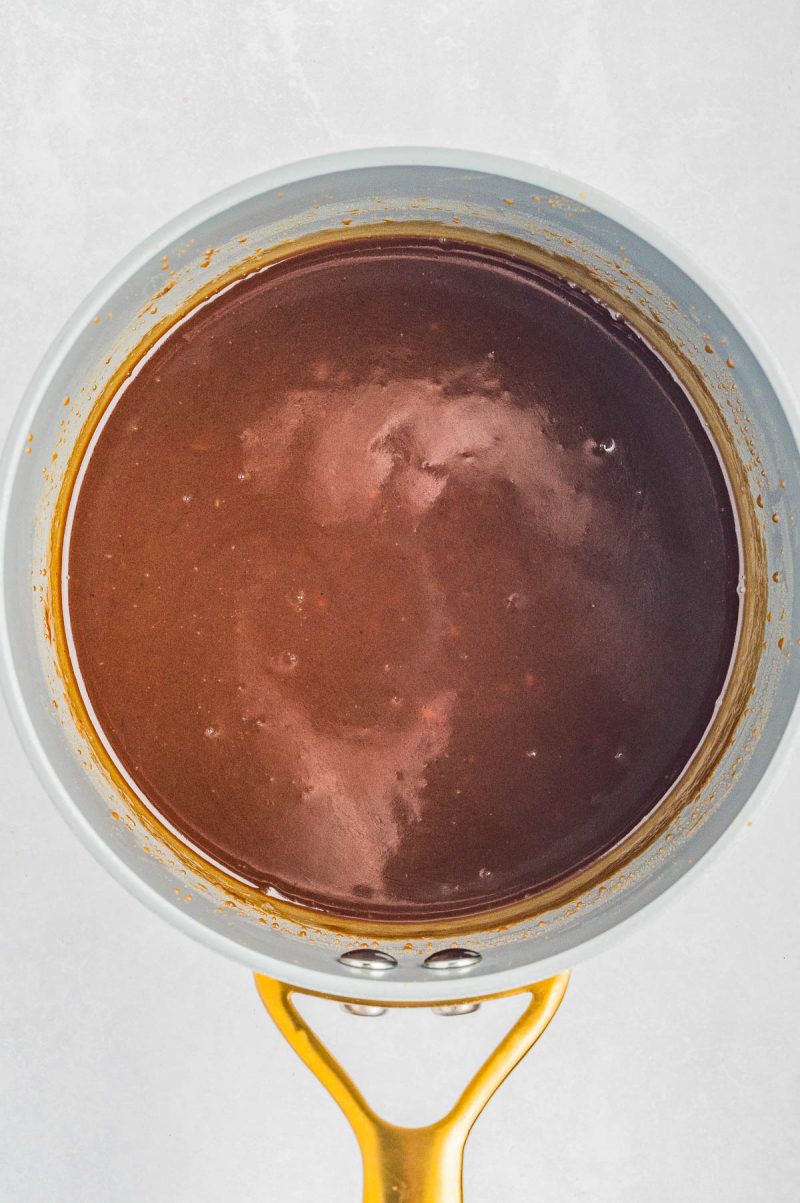 A saucepan filled with a smooth, glossy chocolate sauce viewed from above against a light background.
