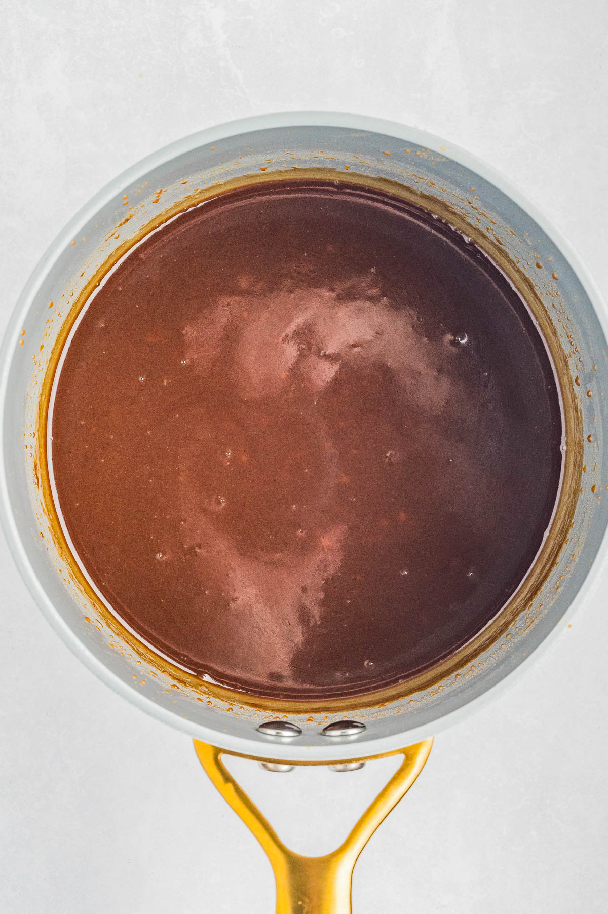 A saucepan filled with a smooth, glossy chocolate sauce viewed from above against a light background.