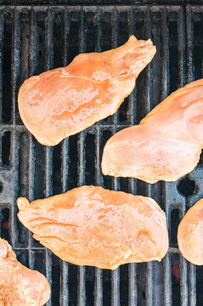 Raw chicken breasts are placed on a grill with visible grill bars beneath.