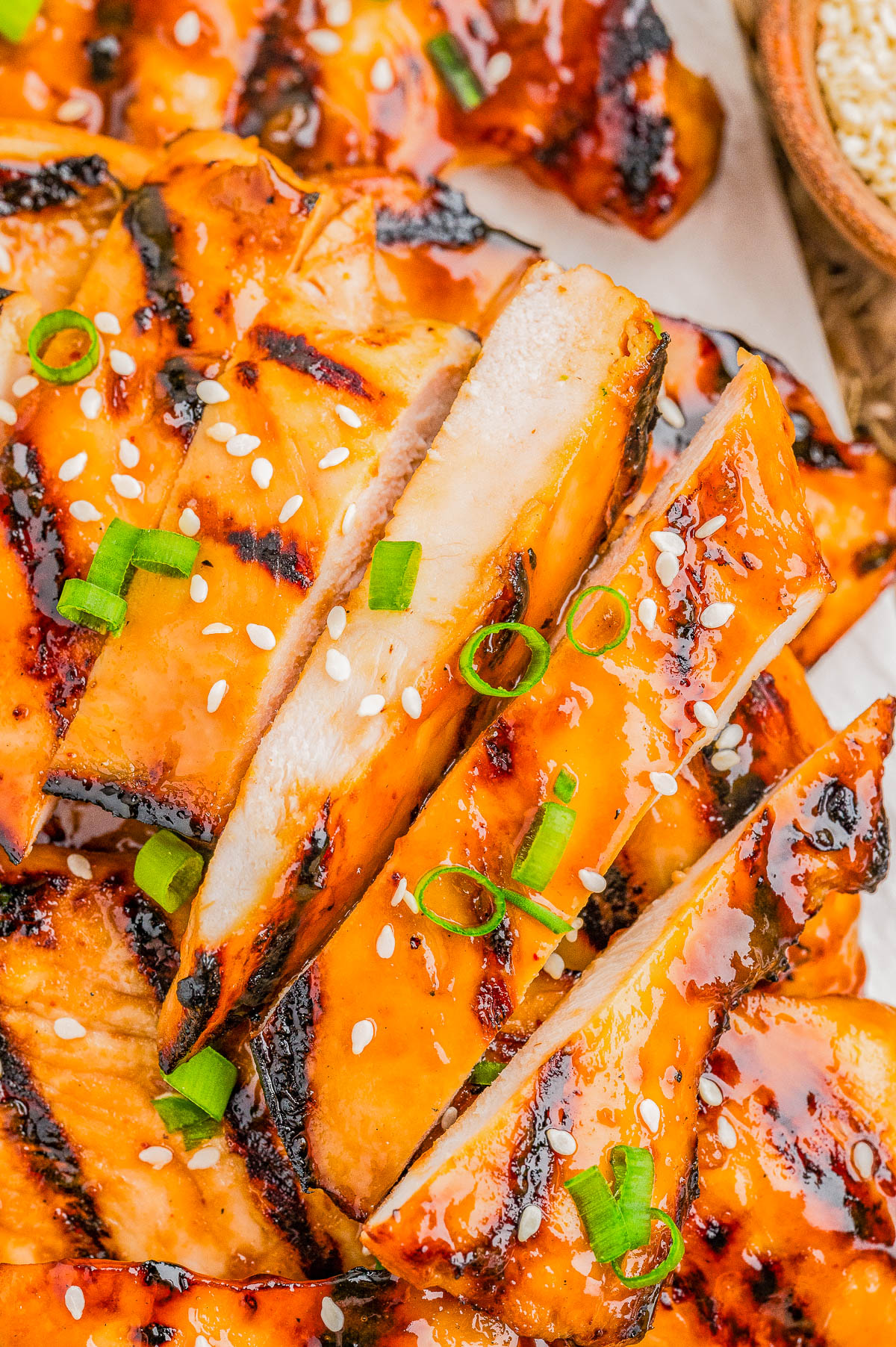 Sliced grilled chicken breast topped with sesame seeds and chopped green onions, showing grill marks and a glossy glaze.