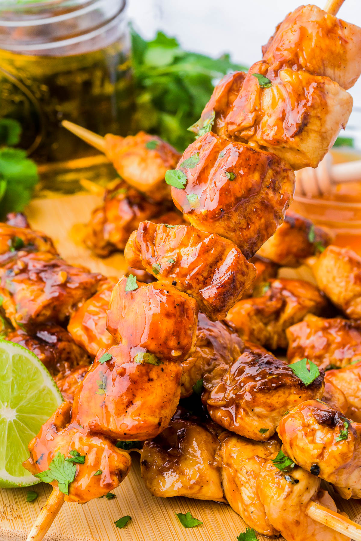 Grilled chicken skewers with a glossy glaze, garnished with chopped herbs, served on a wooden board with lime and cilantro in the background.