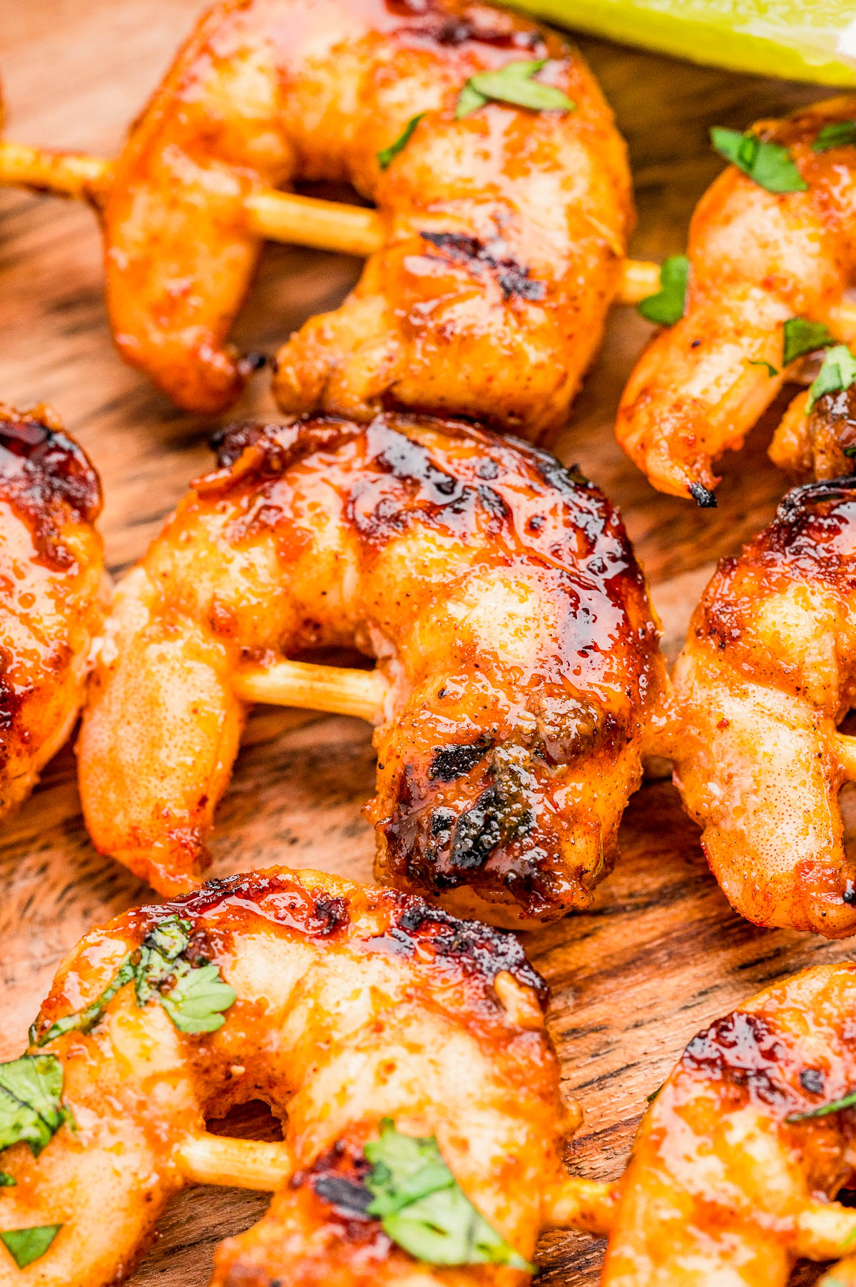 Grilled shrimp skewers with a glaze, garnished with chopped herbs, served on a wooden surface.