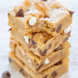 A stack of four thick blondie bars with chocolate chips and white chocolate chunks, with a bite taken out of the top bar.