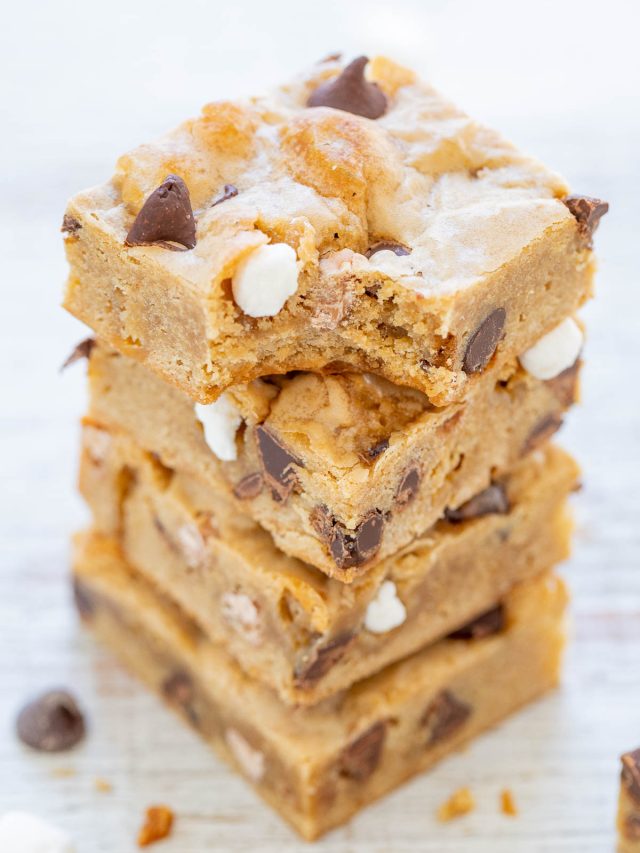 A stack of four thick blondie bars with chocolate chips and white chocolate chunks, with a bite taken out of the top bar.