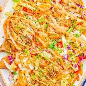A platter of grilled chicken sliced over a colorful salad with cabbage, greens, mandarin oranges, sliced almonds, and a light dressing.