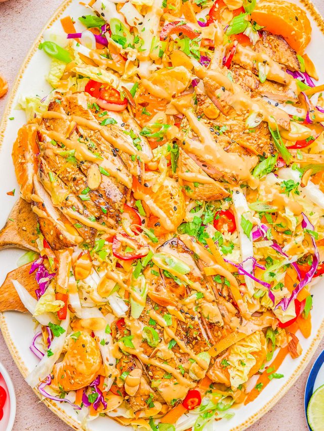 A platter of grilled chicken sliced over a colorful salad with cabbage, greens, mandarin oranges, sliced almonds, and a light dressing.