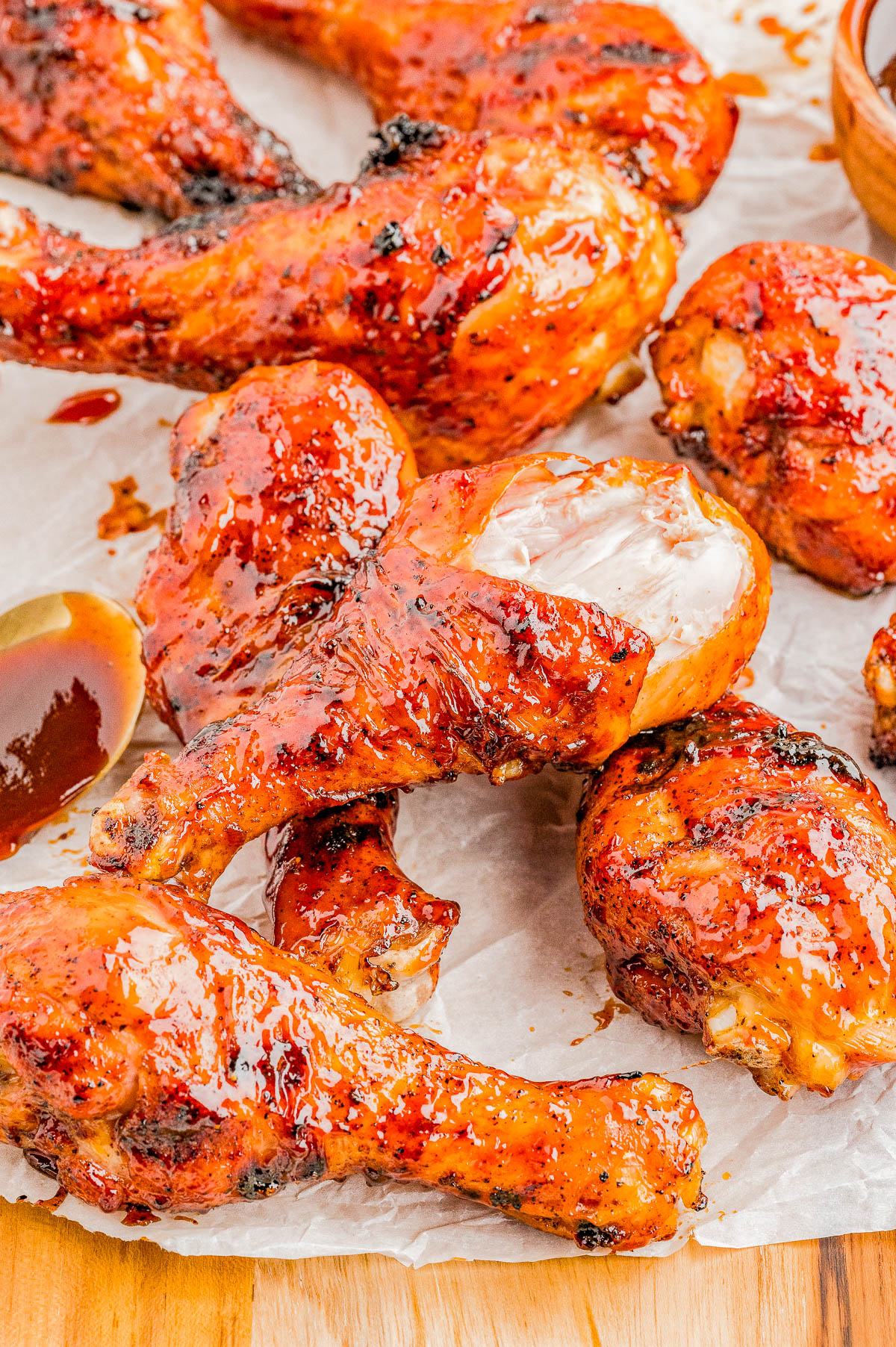 Grilled chicken drumsticks coated in a glossy barbecue sauce, arranged on parchment paper with a spoon and extra sauce nearby.