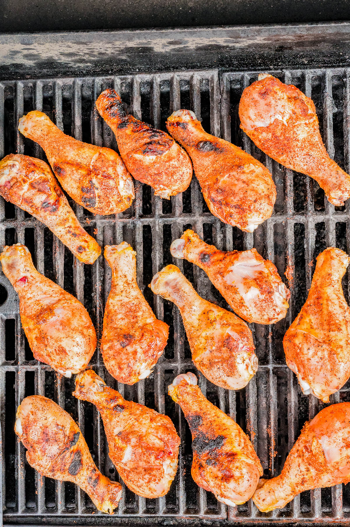 Chicken drumsticks coated with seasoning are arranged and cooking on a grill with visible grill marks.