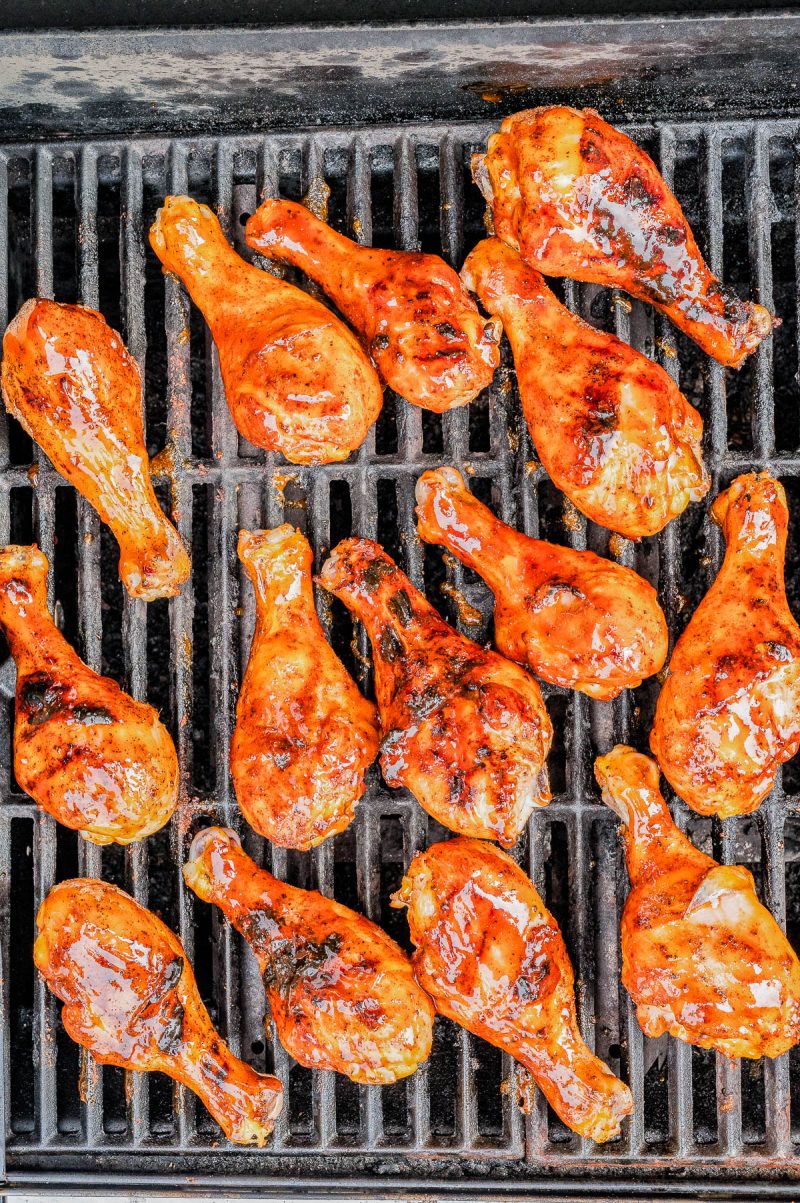 Chicken drumsticks covered in barbecue sauce are being grilled on an outdoor grill.