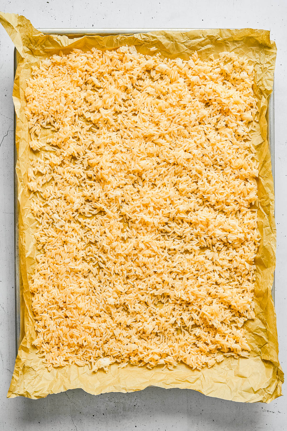 A square baking tray lined with parchment paper holds a single, even layer of grated cheese spread across the surface.