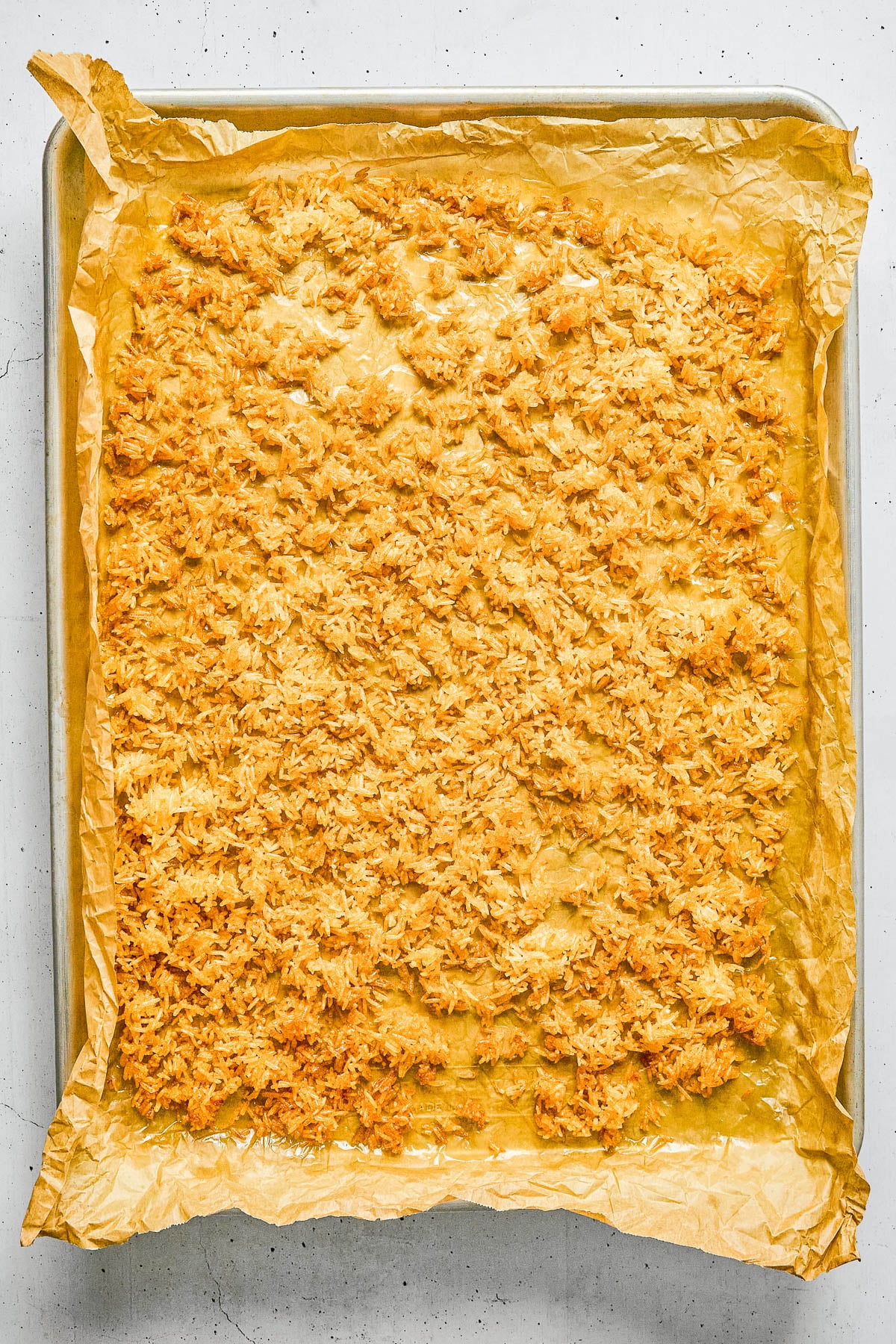 A baking sheet lined with parchment paper holds a large, evenly spread layer of toasted shredded coconut.