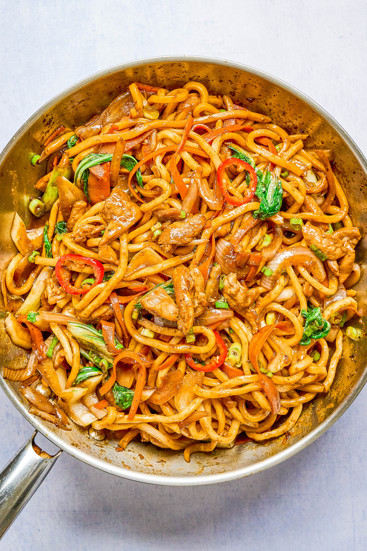A skillet filled with stir-fried noodles, sliced beef, bell peppers, bok choy, onions, and a savory sauce.