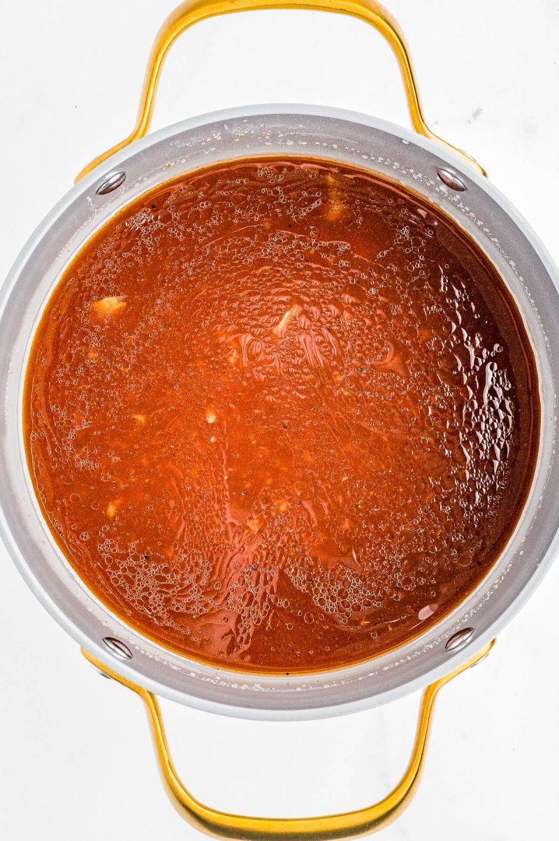 A pot filled with simmering red tomato-based sauce, viewed from above, with gold handles on either side.