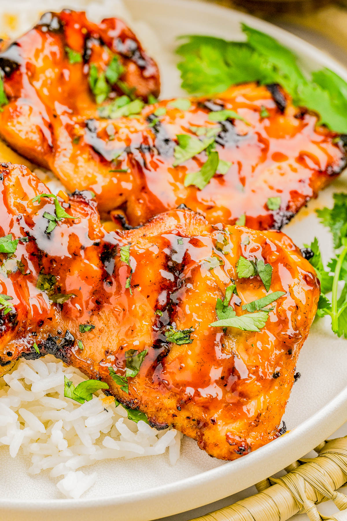 Grilled salmon fillets glazed with a red sauce, garnished with chopped herbs, served over white rice on a plate.