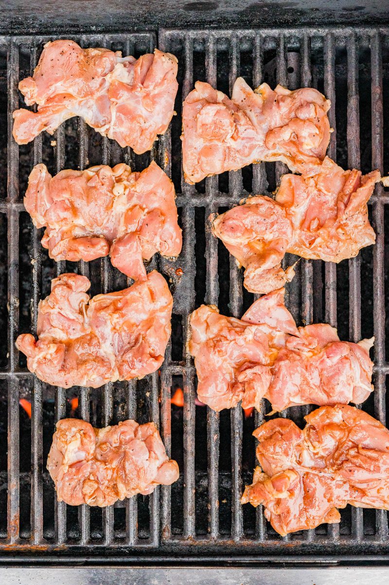 Raw pieces of seasoned chicken arranged on a grill grate over open flames, ready to be cooked.