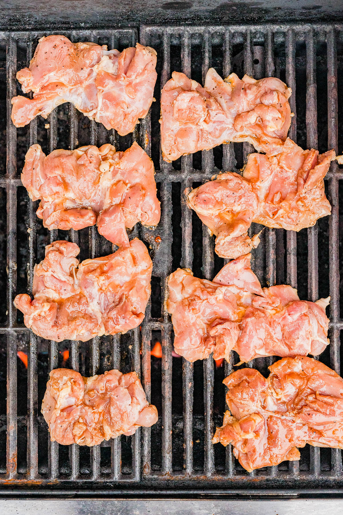 Raw pieces of seasoned chicken arranged on a grill grate over open flames, ready to be cooked.