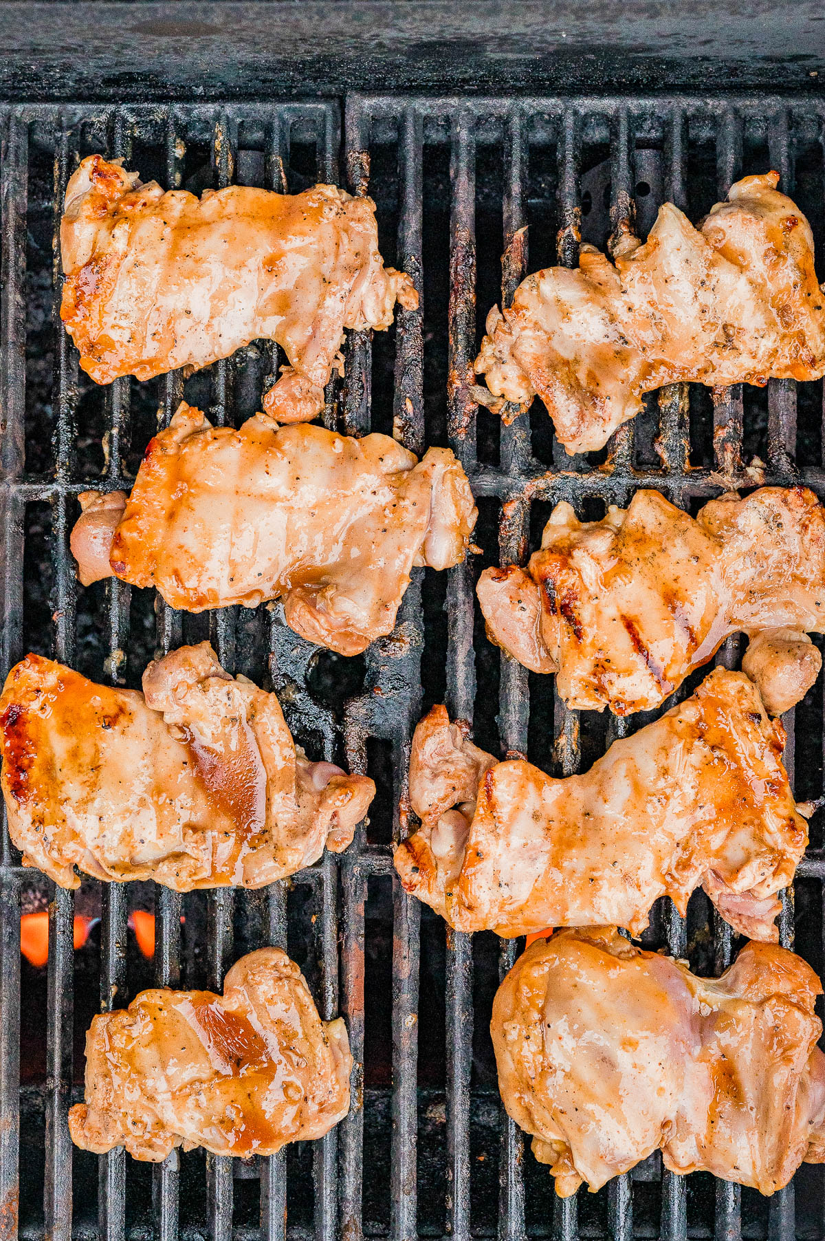 Chicken thighs cooking on a grill with visible grill marks and flames underneath.