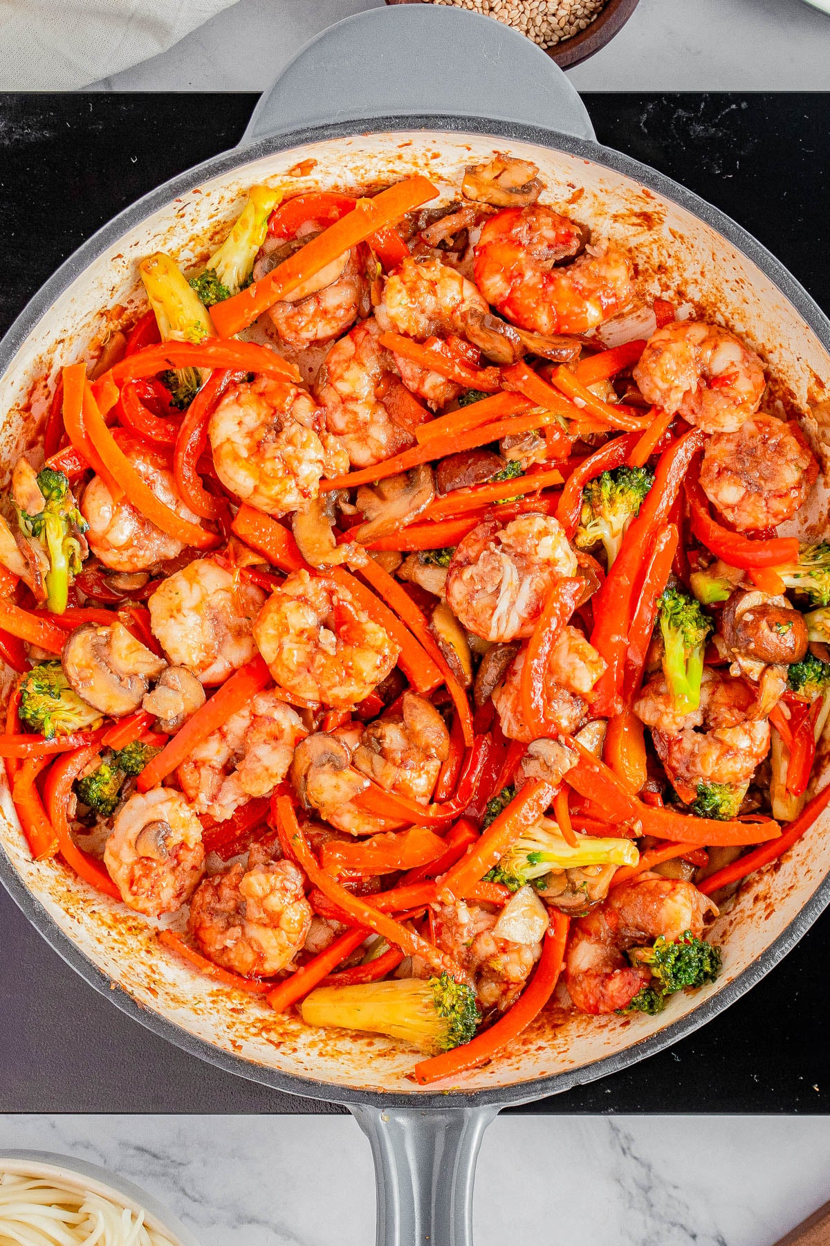 Shrimp stir-fry with broccoli, red bell peppers, mushrooms, and carrots in a large pan on a stovetop.