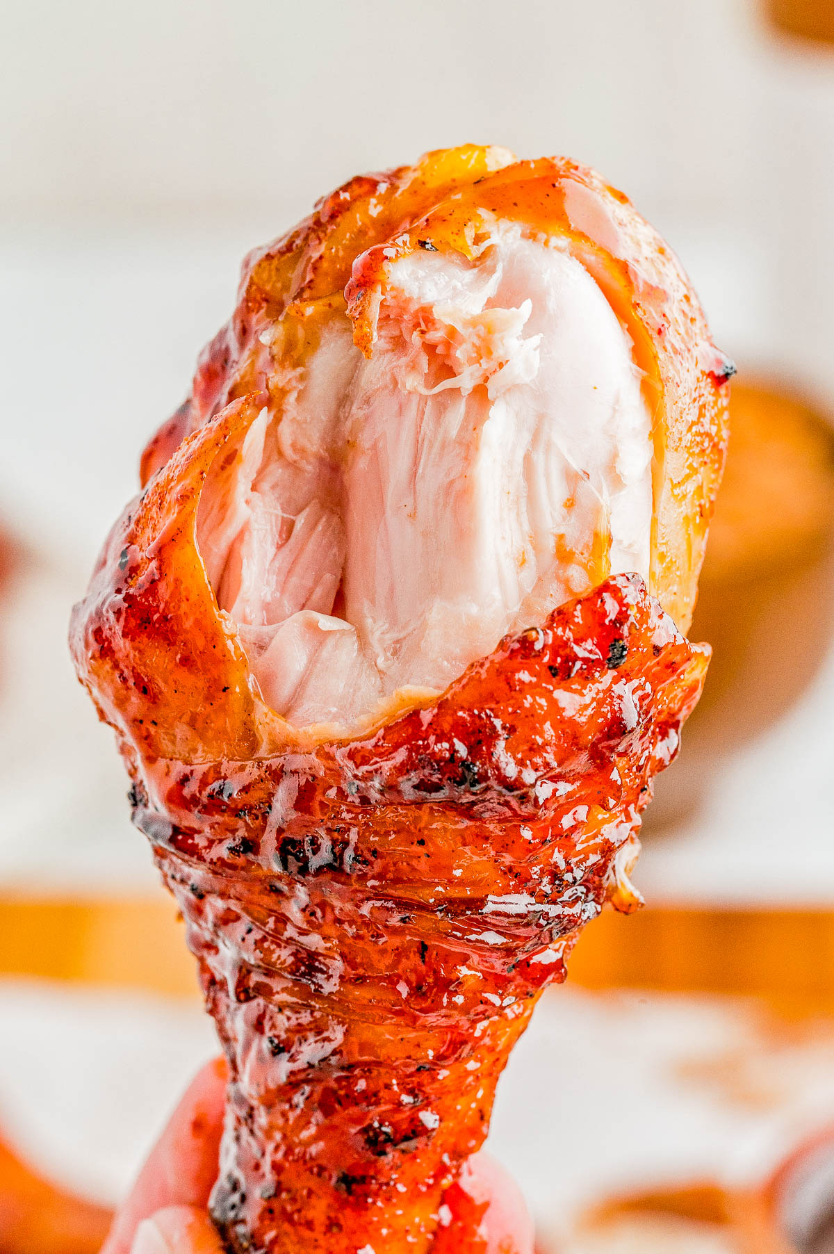 A close-up of a cooked chicken drumstick with a bite taken out, showing the juicy white meat and crispy, seasoned skin.