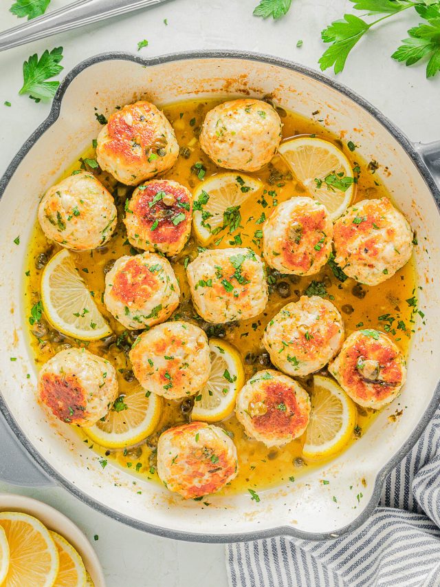 A skillet filled with browned chicken meatballs in a lemon sauce, garnished with lemon slices and chopped parsley.