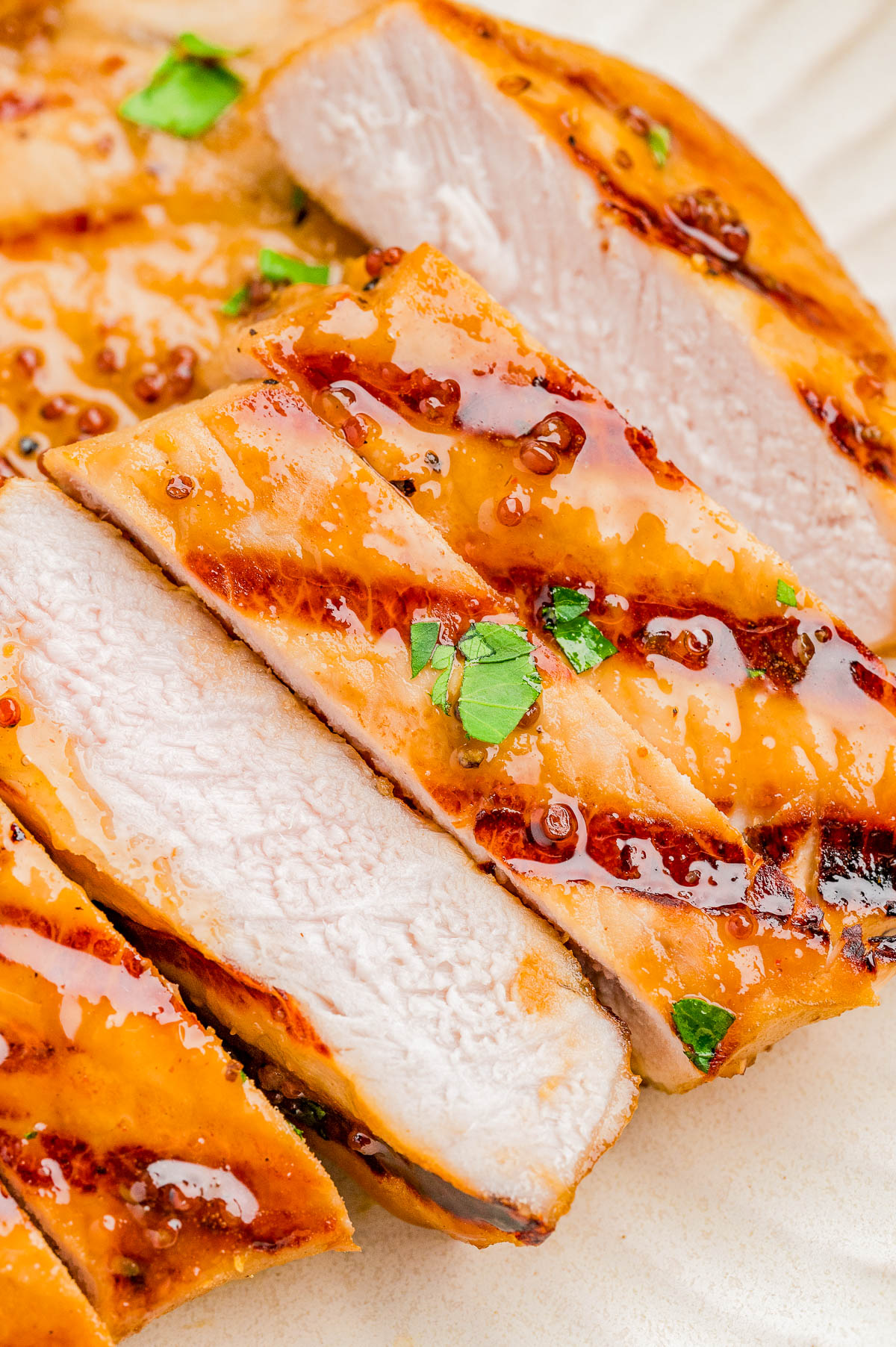 Close-up of sliced, grilled pork chops topped with a glossy sauce and garnished with chopped herbs.