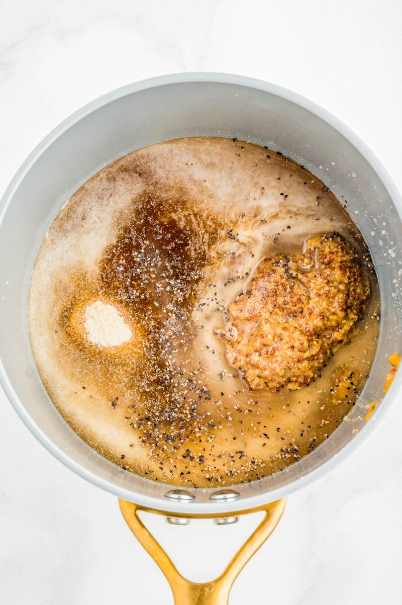 A saucepan containing mustard, seasonings, and liquid ingredients, viewed from above, prior to mixing.