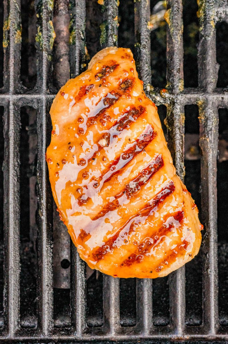 A glazed piece of grilled chicken breast with visible grill marks sits on a metal grill grate.