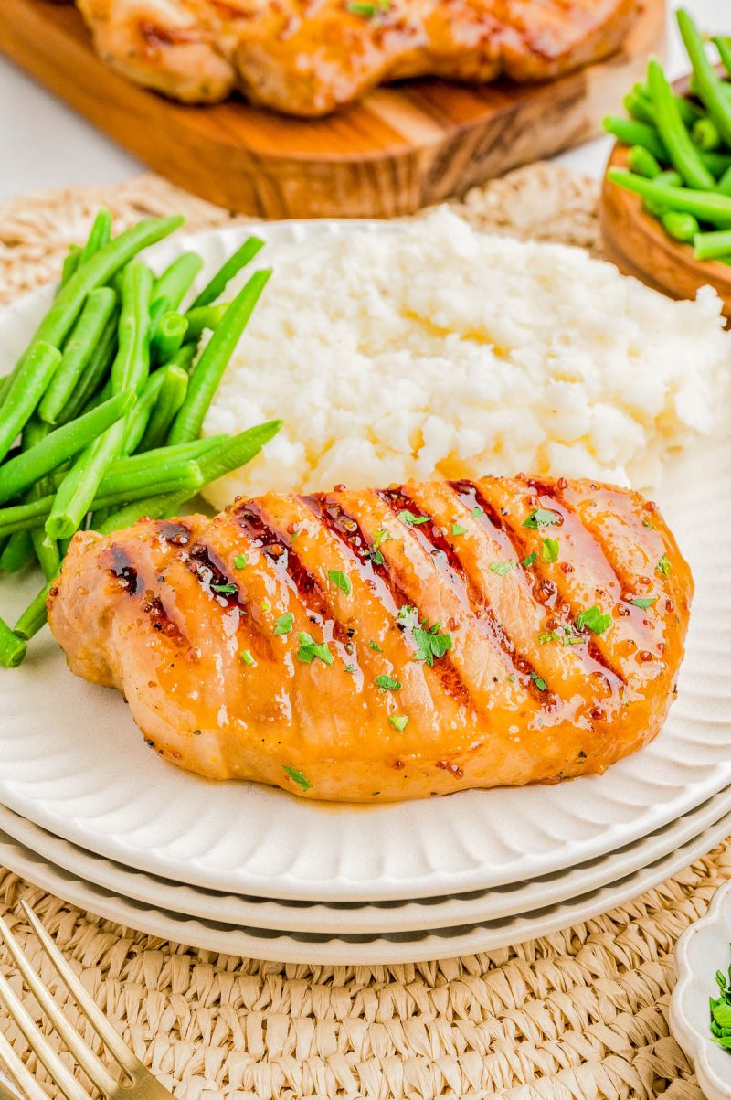 Grilled chicken breast with grill marks, served with green beans and mashed potatoes on a white plate.
