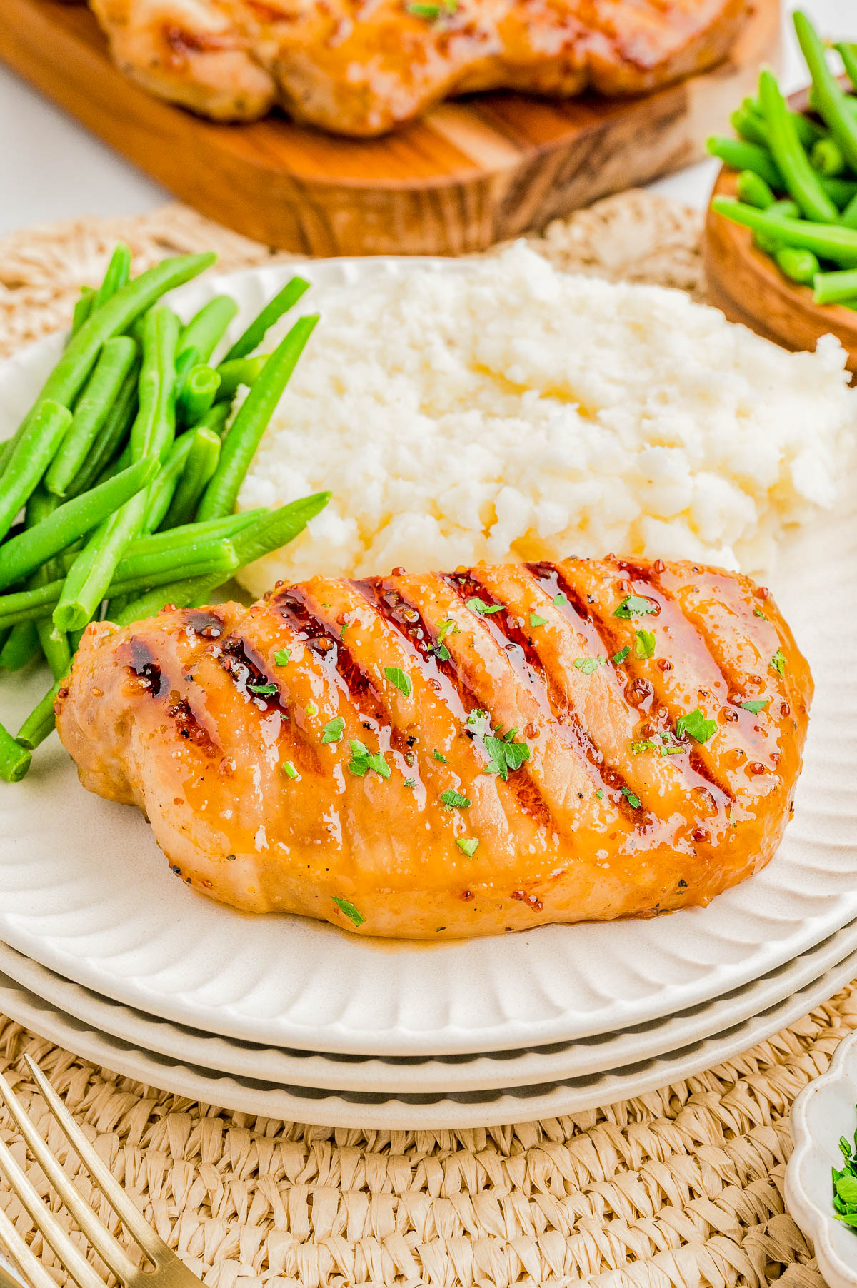 Grilled chicken breast with grill marks, served with green beans and mashed potatoes on a white plate.