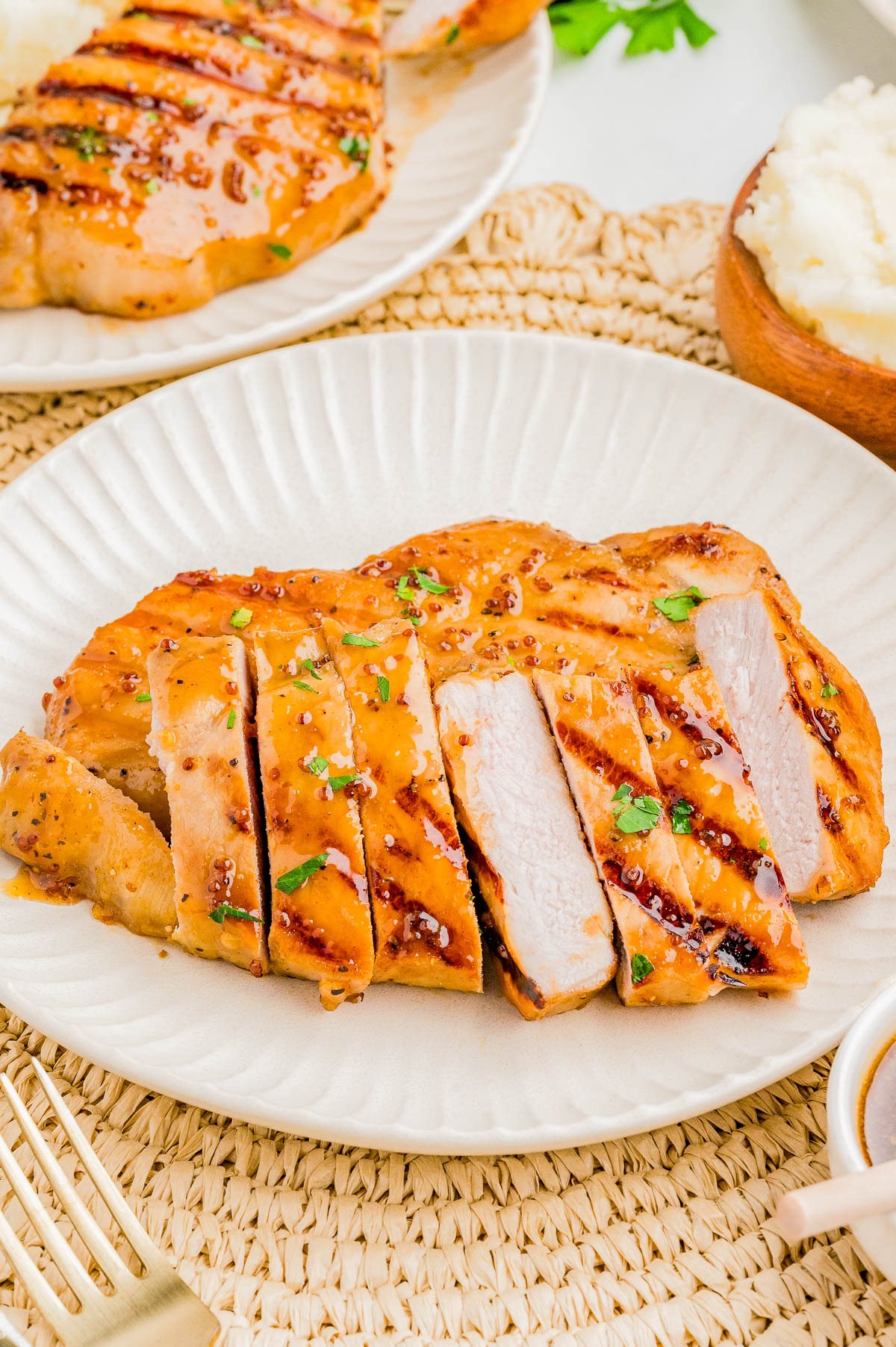 Sliced grilled chicken breast garnished with chopped herbs, served on a white plate.