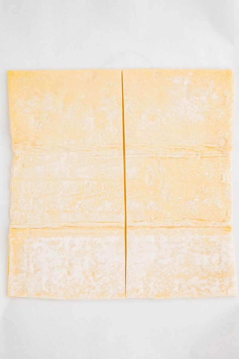 Four rectangular sheets of raw pasta dough, lightly dusted with flour, are arranged on a white surface.