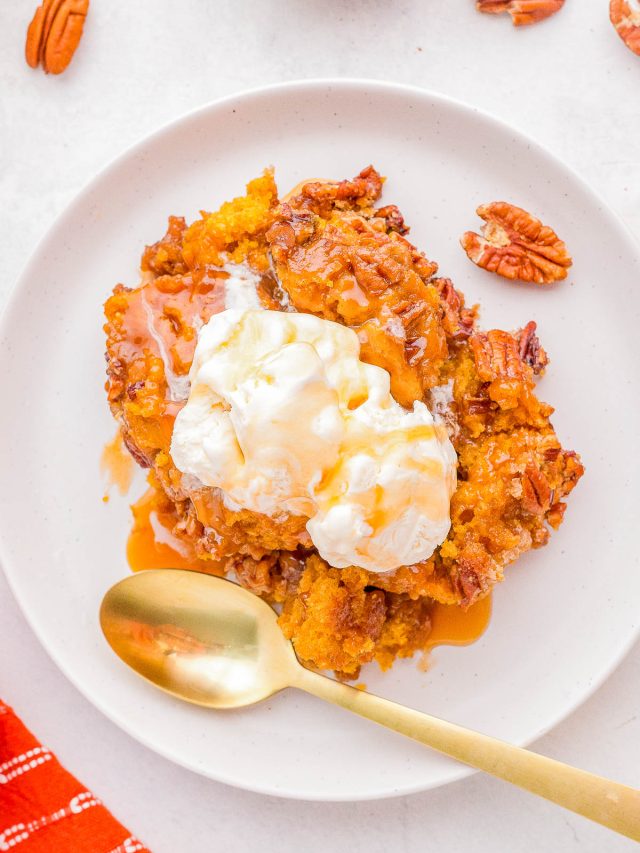 A serving of pumpkin dessert topped with a scoop of vanilla ice cream and drizzled with caramel sauce, garnished with pecans, on a white plate with a gold spoon.