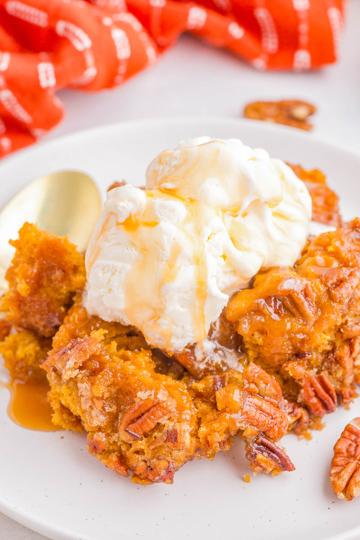 A serving of pecan dessert topped with a scoop of vanilla ice cream and drizzled with caramel sauce on a white plate.