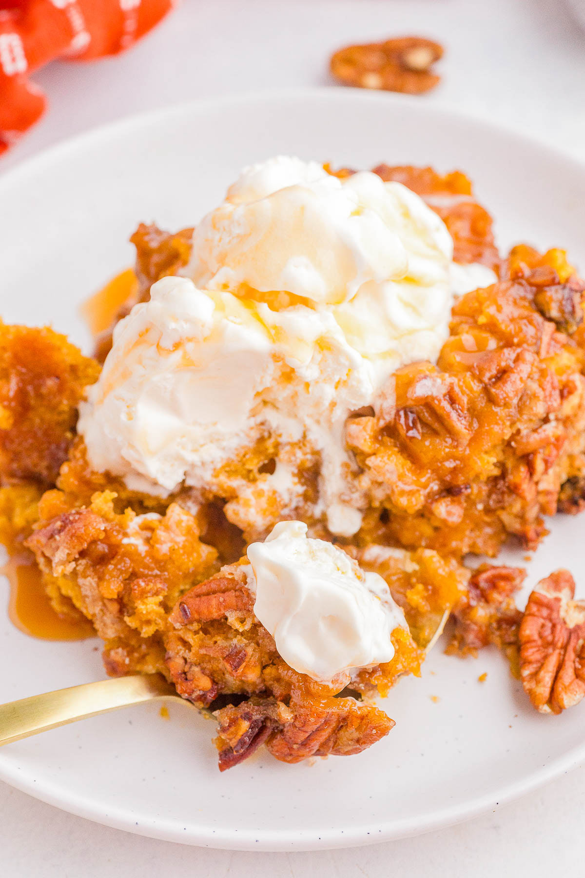 A serving of pumpkin pecan dessert topped with vanilla ice cream and caramel sauce on a white plate with a fork.