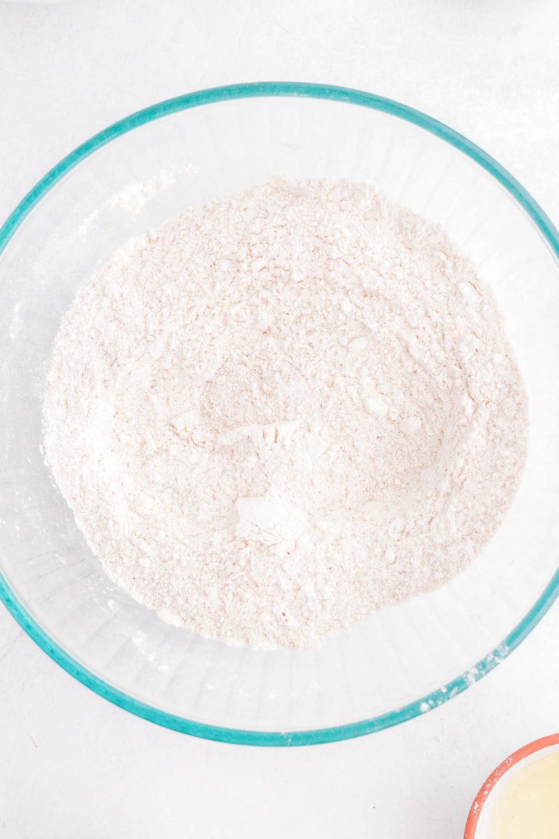 A glass bowl filled with a mixture of dry, white flour on a light-colored surface.