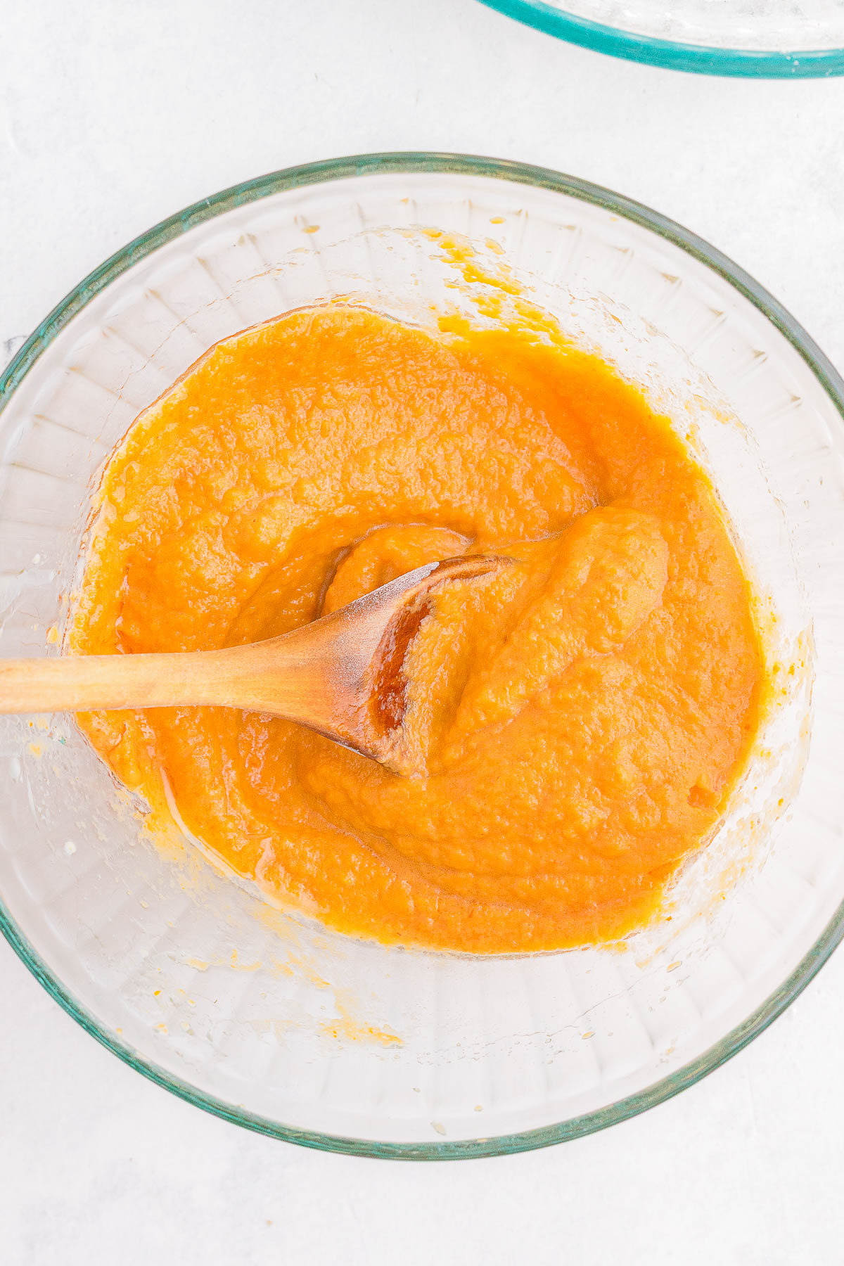 A glass bowl filled with orange pumpkin puree being stirred with a wooden spoon.