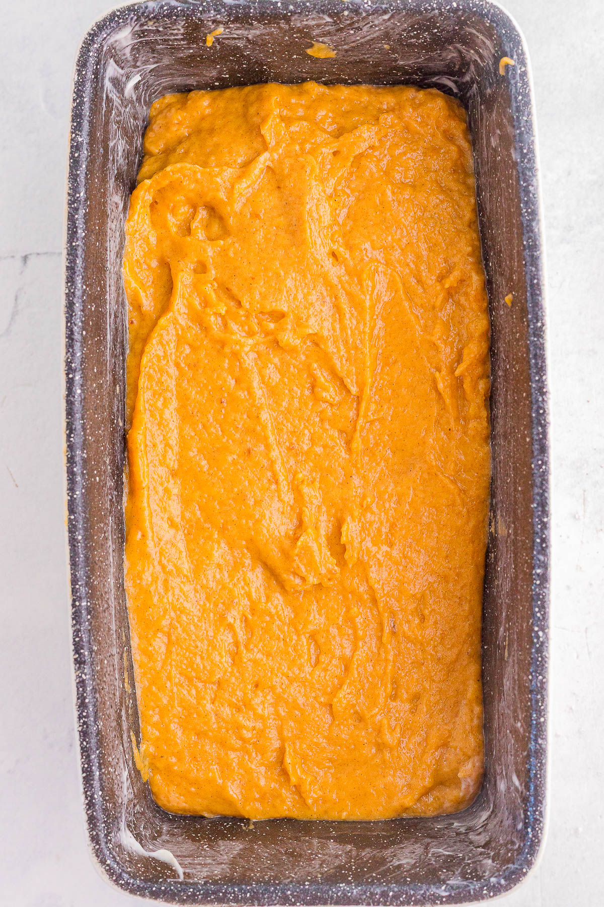 A loaf pan filled with unbaked orange pumpkin bread batter, ready to be baked.