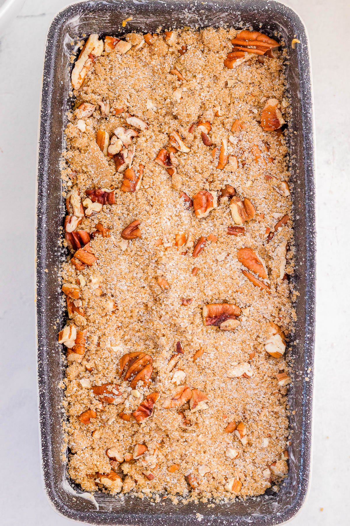 A rectangular loaf pan filled with unbaked crumb topping and chopped pecans on top, ready for baking.