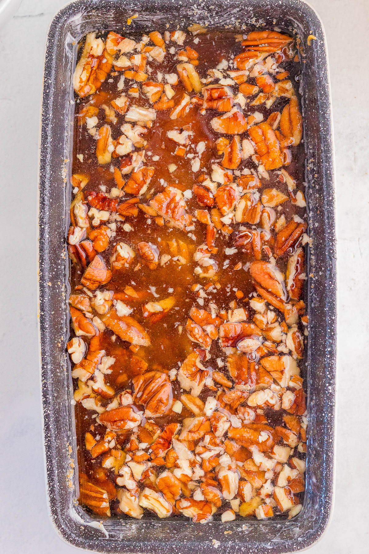 A rectangular baking pan filled with a mixture of chopped pecans and caramel sauce, ready for baking.