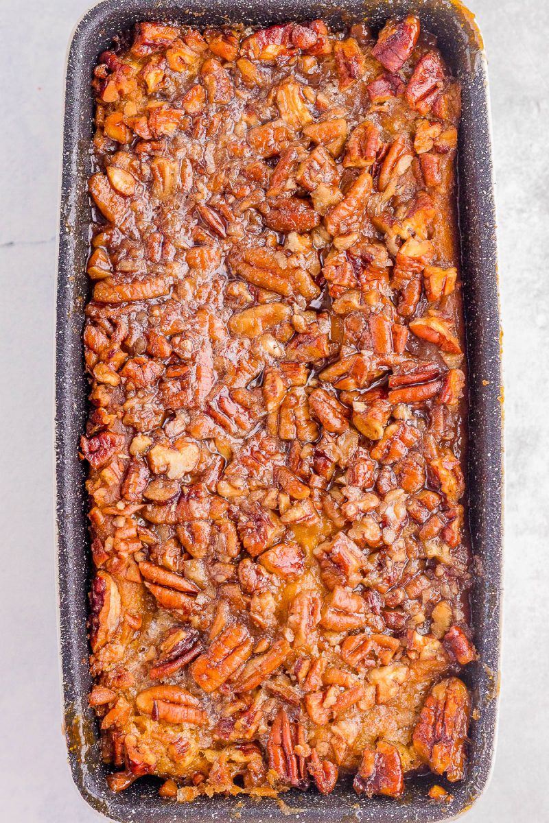 A rectangular loaf pan filled with bread pudding topped with chopped pecans and a caramelized glaze.