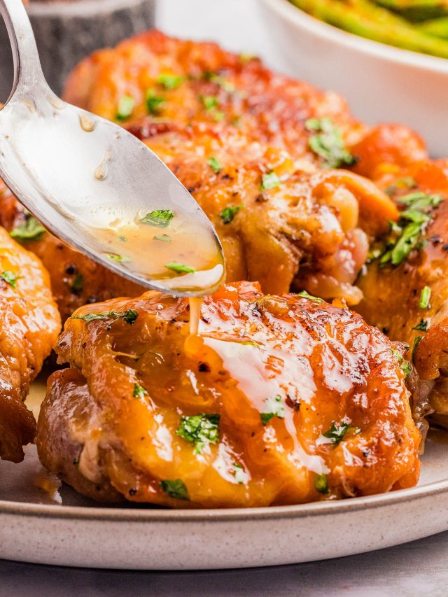 A spoon drizzles sauce over a piece of cooked, golden-brown chicken garnished with chopped herbs on a plate.