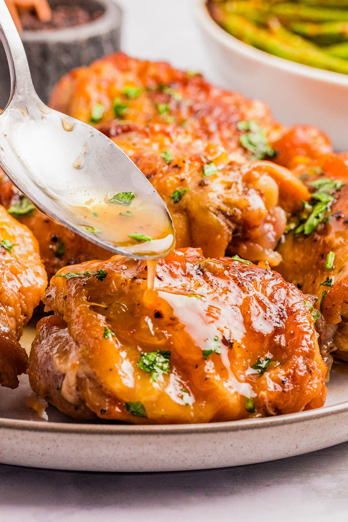 A spoon drizzles sauce over a piece of cooked, golden-brown chicken garnished with chopped herbs on a plate.