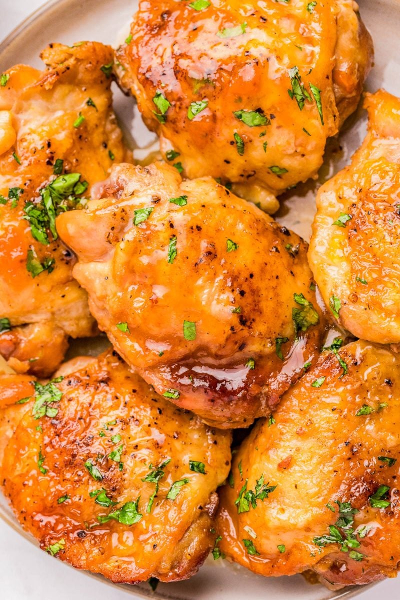Close-up of several pieces of glazed, golden-brown cooked chicken garnished with chopped fresh herbs on a plate.