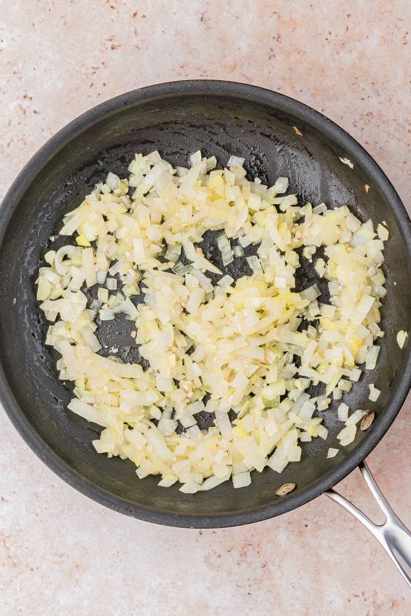 Chopped onions being sautéed in a black frying pan on a light-colored countertop.