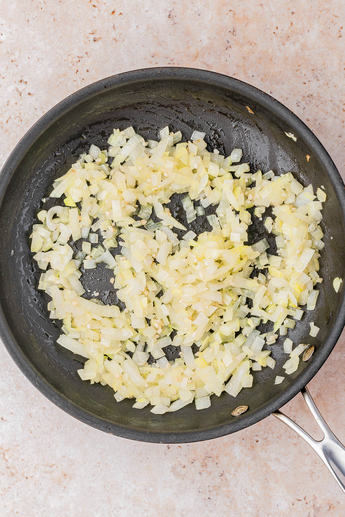 Chopped onions being sautéed in a black frying pan on a light-colored countertop.