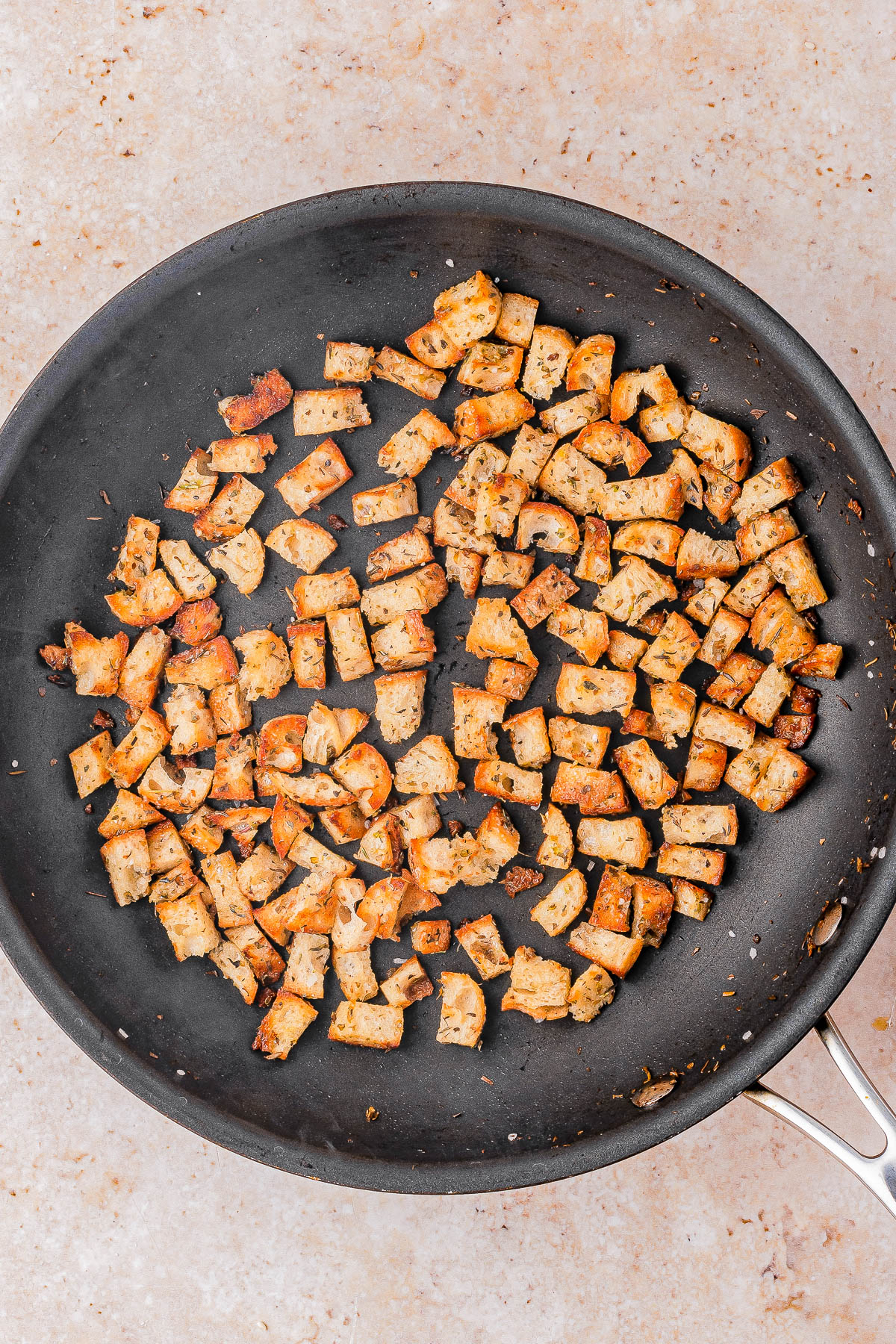 Small, seasoned tofu cubes are cooked evenly in a black nonstick skillet placed on a light-colored countertop.