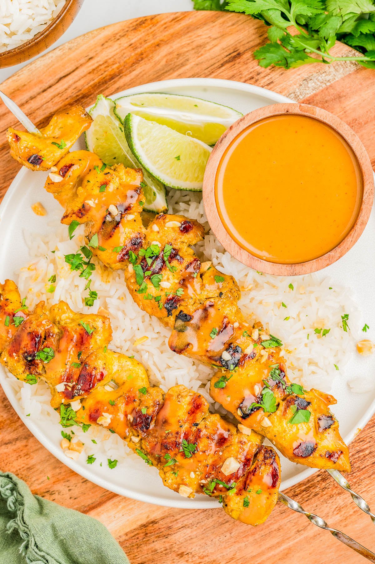 Two grilled chicken skewers on white rice, garnished with herbs, served with lime wedges and a small bowl of orange dipping sauce on a white plate.
