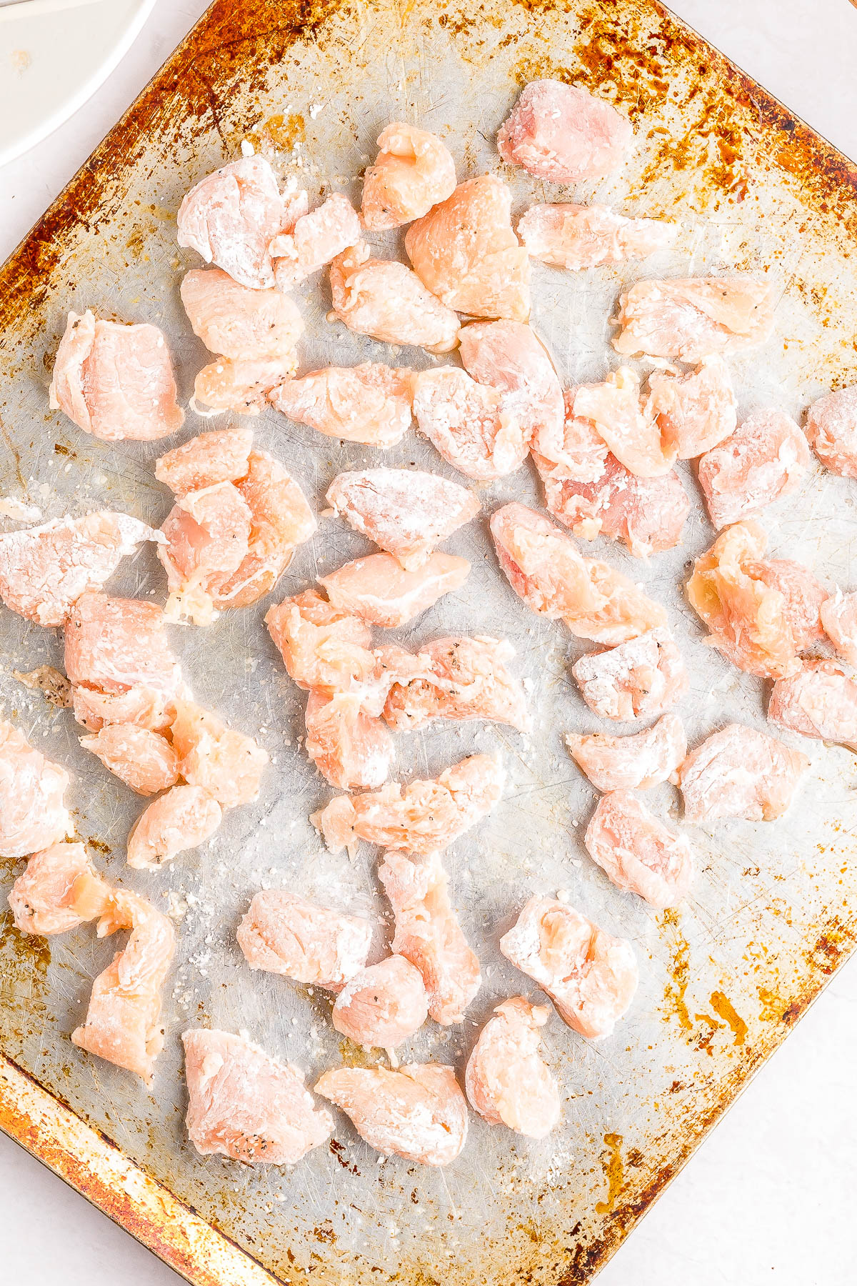Raw, flour-coated chicken pieces spread out on a well-used baking sheet.
