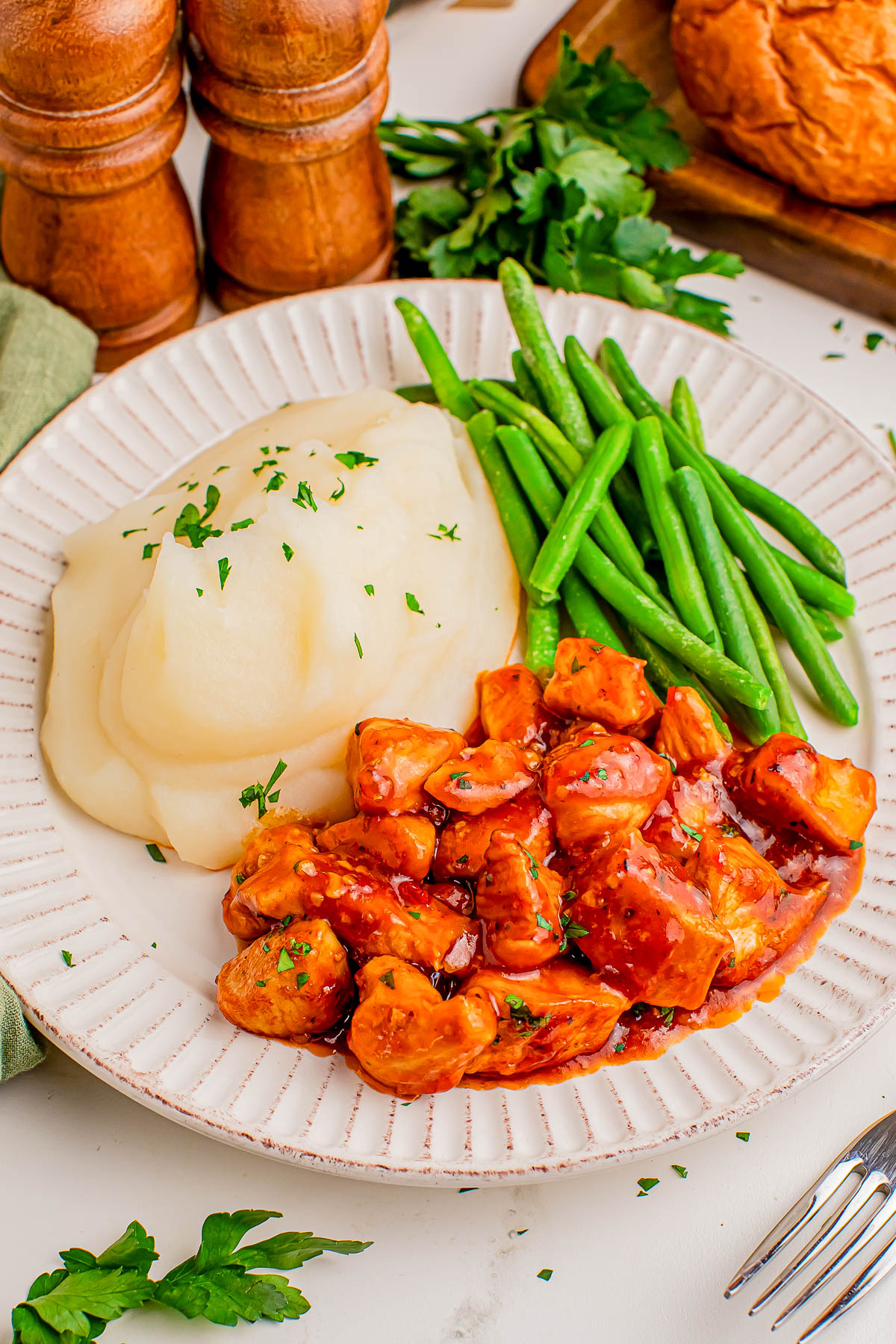 A plate with mashed potatoes, green beans, and diced chicken in a red sauce, garnished with chopped herbs.